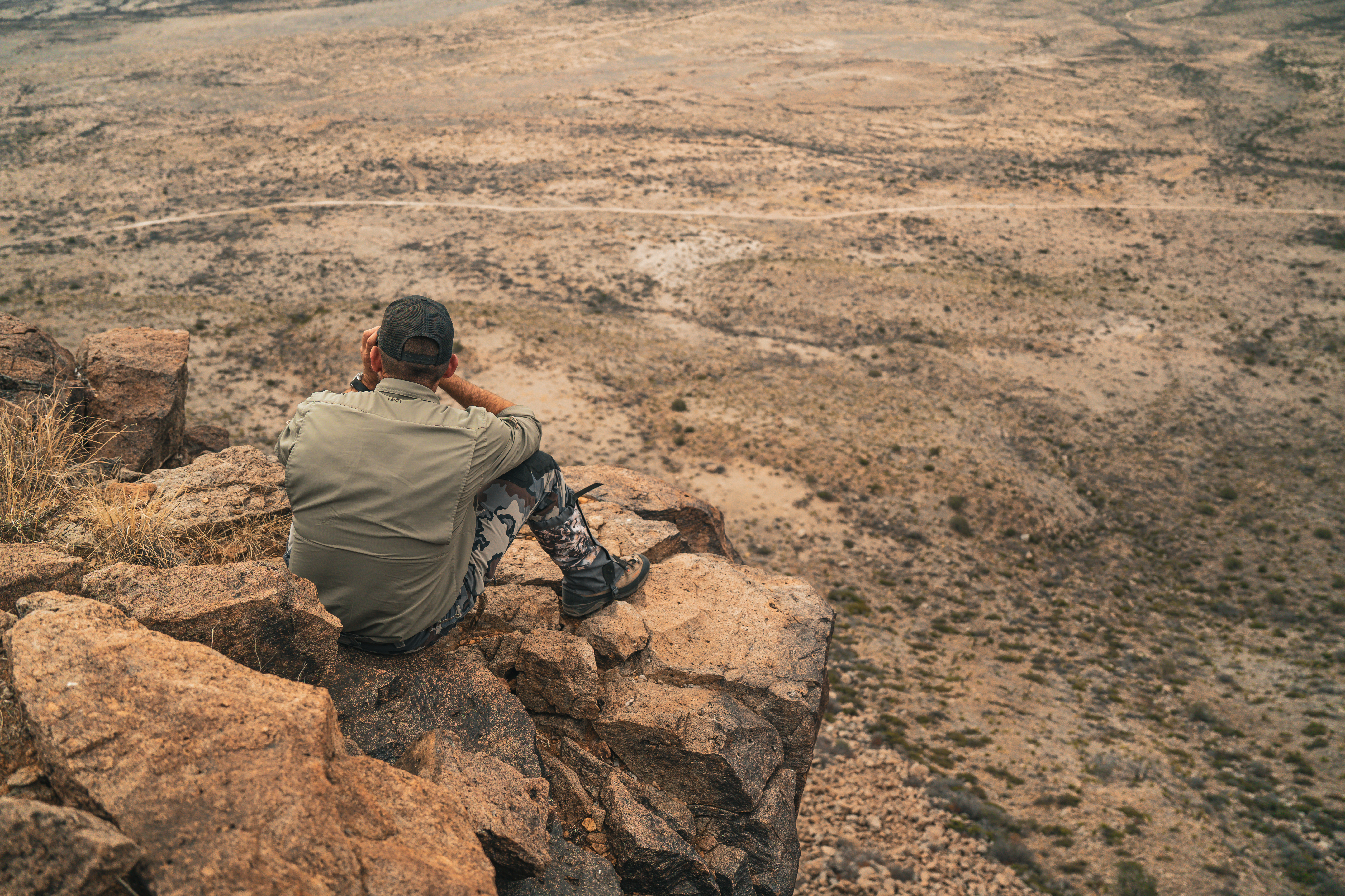 Hunter overlooking desert landscape from rock ledge